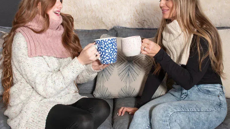 Two women in cozy knitwear enjoying coffee on a stylish sofa, Love Classic home style