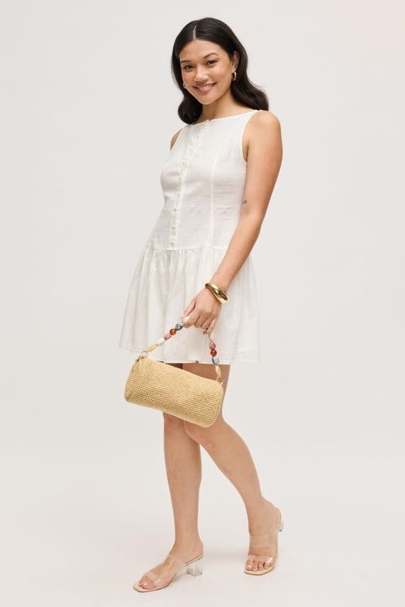 Model wearing the natural Rachel Straw Clutch styled as a crossbody with its detachable chain, detailed bead accents, and secure zip-top closure.