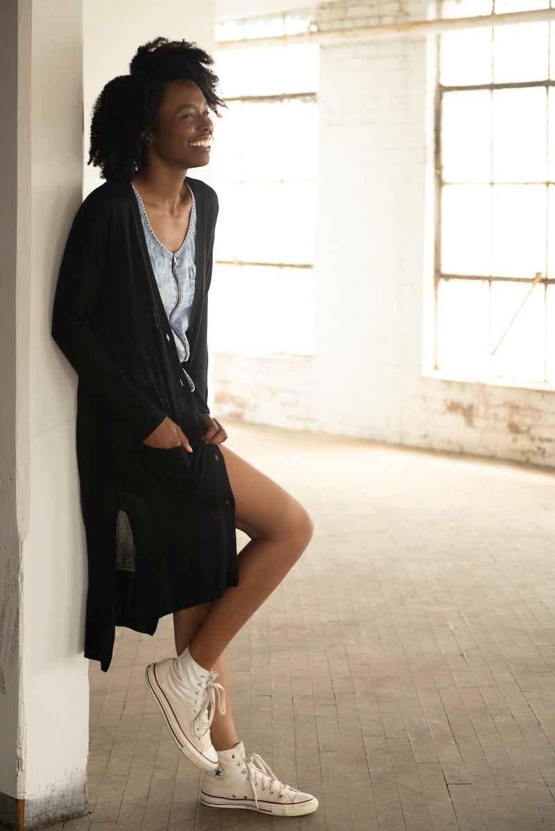 Smiling woman in Love Classic casual denim dress and black cardigan, white high-top sneakers, indoors