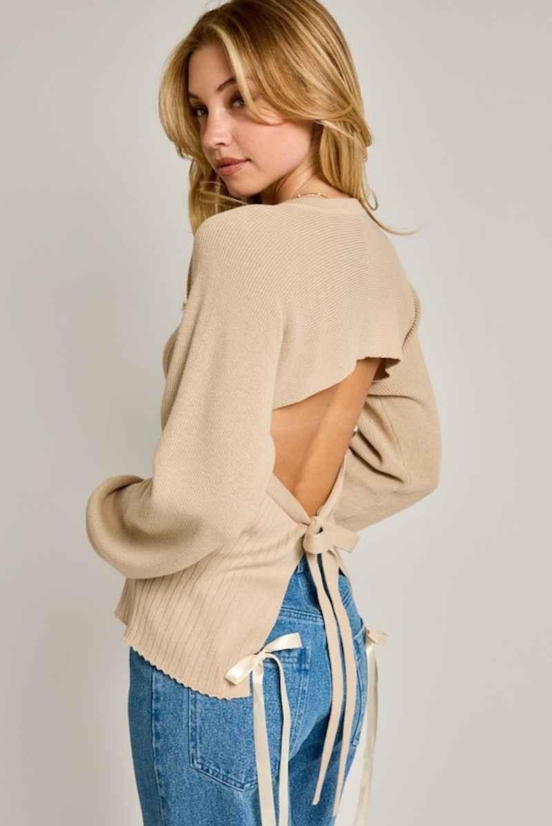 Woman wearing beige open-back sweater with ribbon ties and blue jeans, Love Classic fashion style