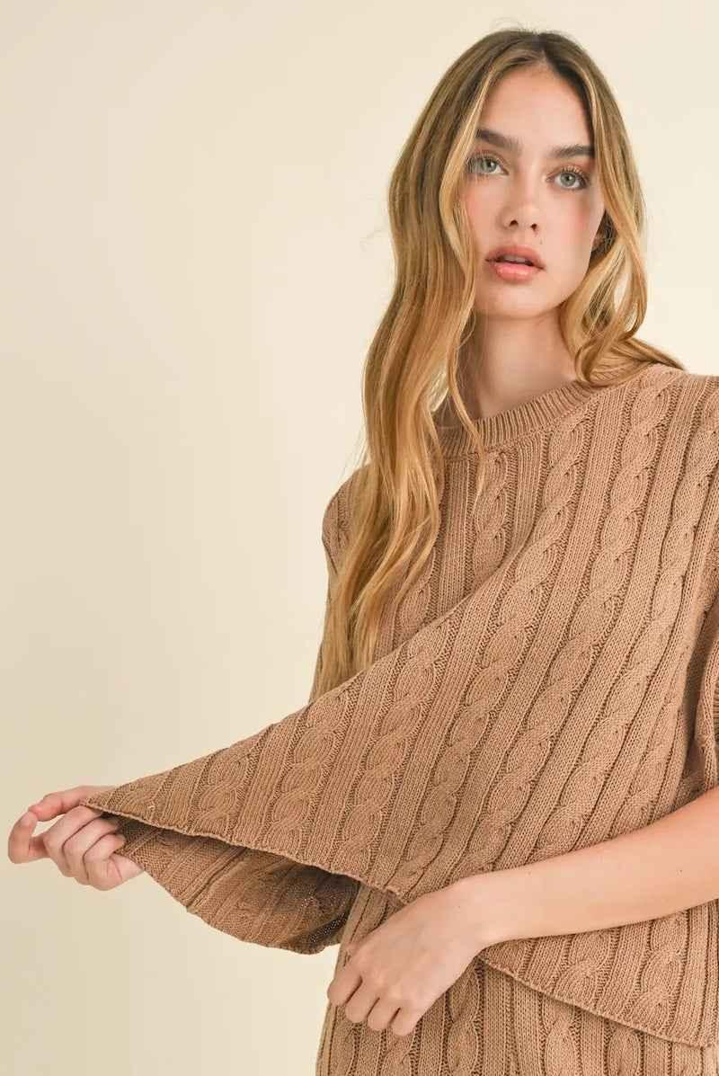 Woman modeling a beige cable knit sweater from Love Classic, soft neutral background