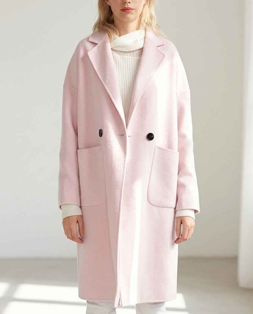 Close-up view of the Publisher Double-Breasted Wool Blend Coat in blush pink, showcasing its wool-blend texture, structured notched lapels, double-breasted front buttons, oversized front patch pockets, and relaxed fit layered over a ribbed cream sweater in a bright indoor setting.