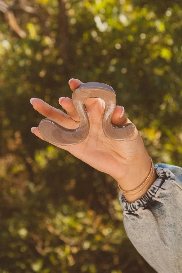 Hand holding a wavy, taupe-colored hair clip outdoors, Love Classic style accessory