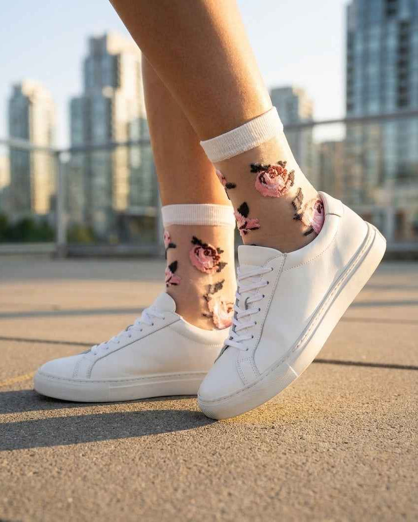 Roses Sheer Socks 2-Pack featuring sheer ankle socks with raised rose embroidery and soft ribbed cuffs, worn with white sneakers in an outdoor city setting, highlighting the delicate floral pattern and light transparent texture.