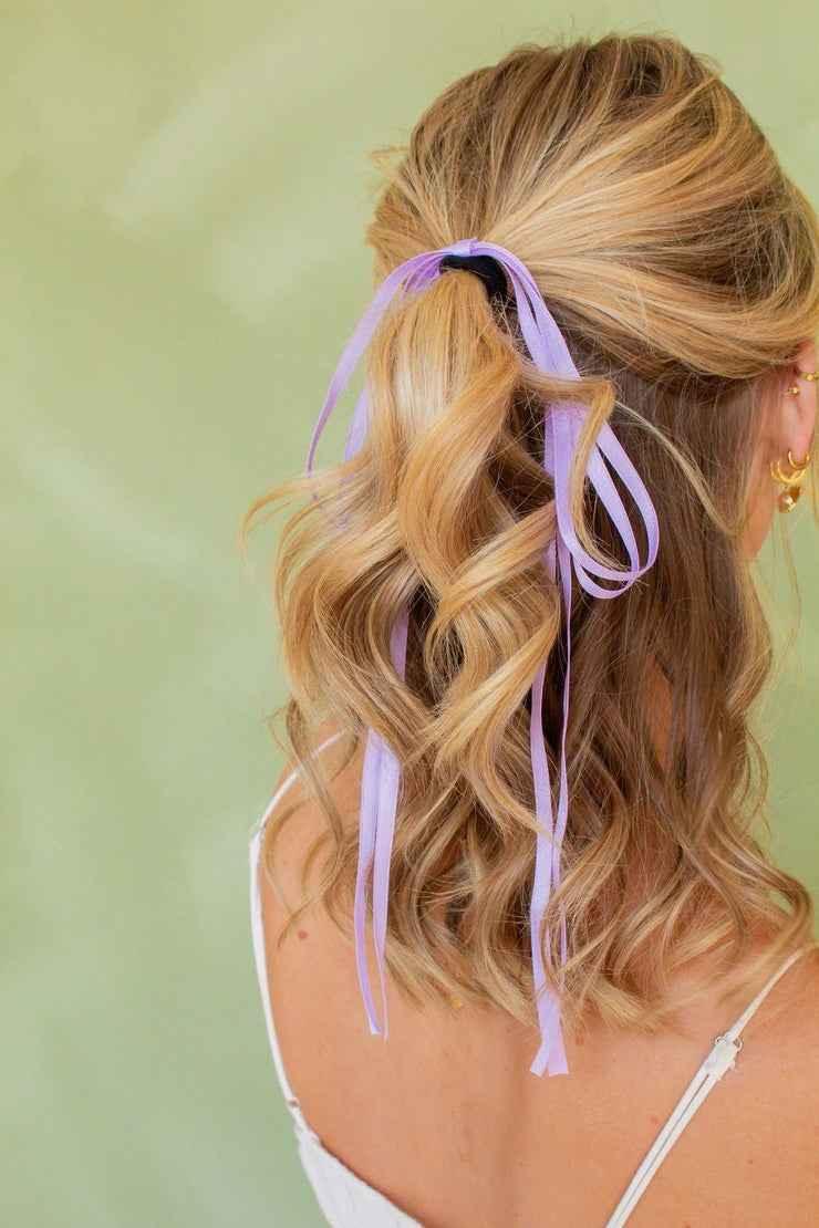 Back view of wavy blonde hair with a lavender ribbon, stylish look from Love Classic