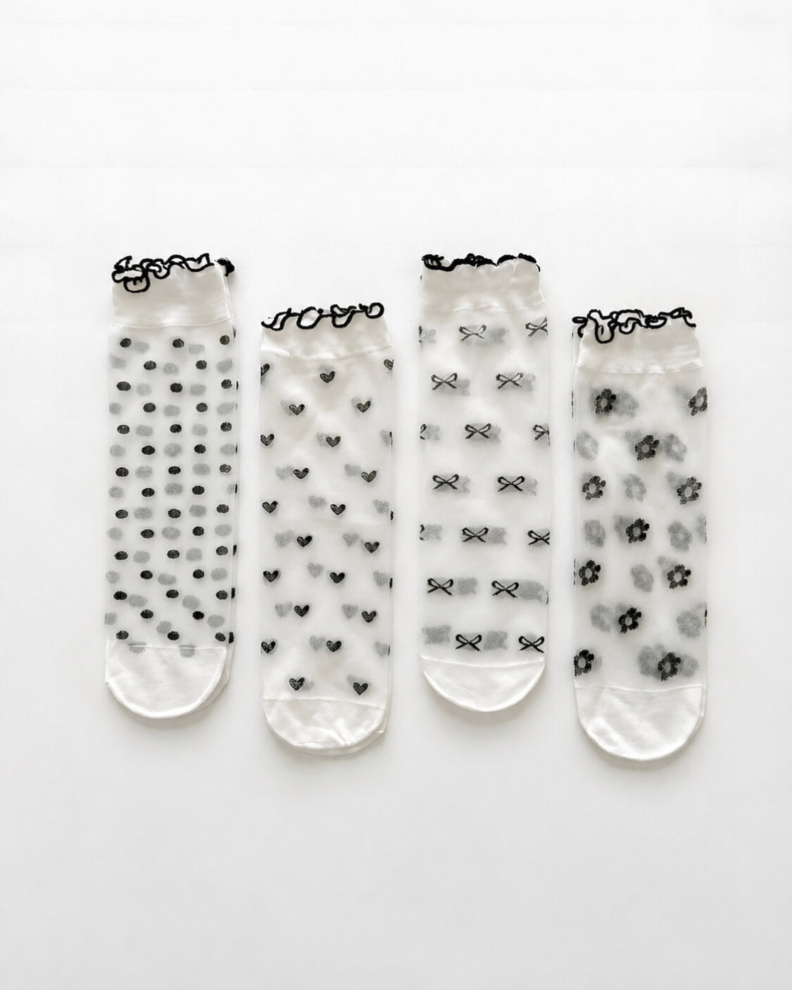 4-Pack Geo Print Ruffle Edge Sheer Socks featuring four unique transparent sock styles with polka dot, heart, bow, and floral-inspired geometric patterns, finished with contrasting ruffle-edge cuffs and displayed on a clean white background to showcase variety, lightweight construction, and coordinated styling.