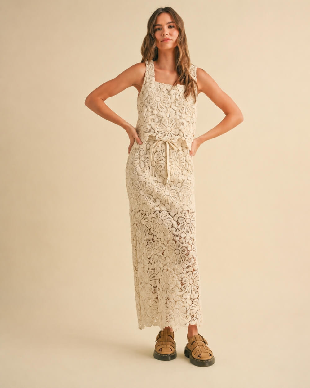 Crochet Knitted Skirt featuring a sleeveless layered silhouette with intricate floral crochet patterns and an adjustable drawstring waist, styled with woven buckle sandals in a full front standing pose against a soft neutral studio backdrop, highlighting relaxed texture and flowing movement.