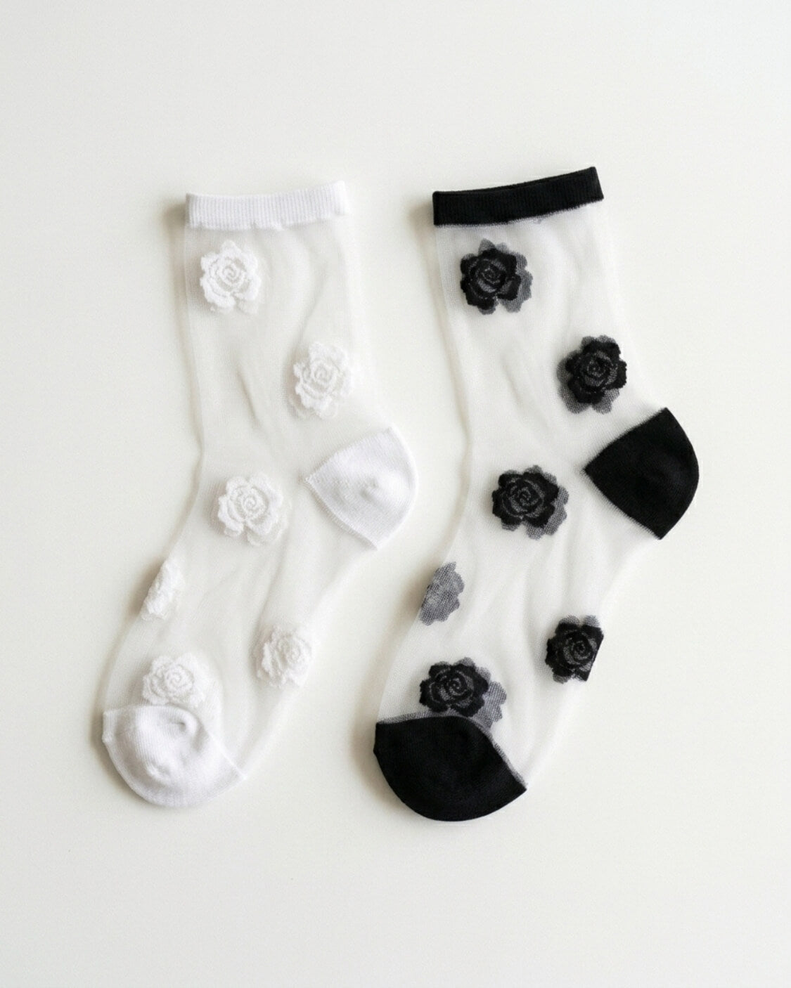 2-Pack Rosette Mesh Crew Socks featuring one white pair with white rosette embroidery and one black-trimmed pair with black rosette embroidery, displayed side by side on a clean white background, highlighting the sheer mesh construction and elegant floral detailing for versatile everyday styling.