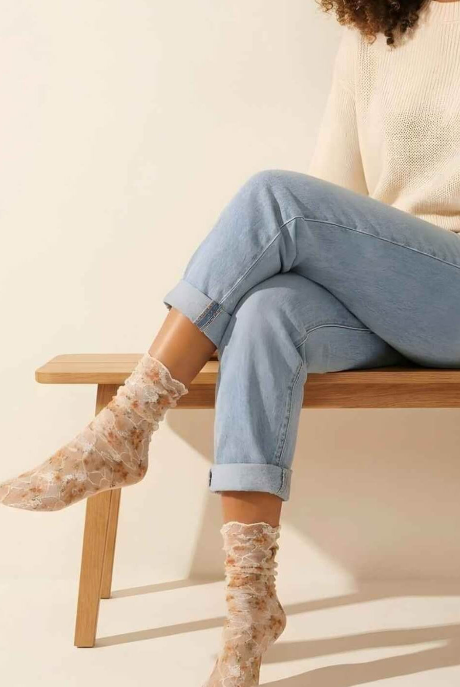 Floral mesh sheer socks in orange with delicate lace overlay and soft floral print, styled with rolled cuff jeans and a knit sweater while seated on a wooden bench, highlighting the lightweight, semi-transparent fabric and feminine design.
