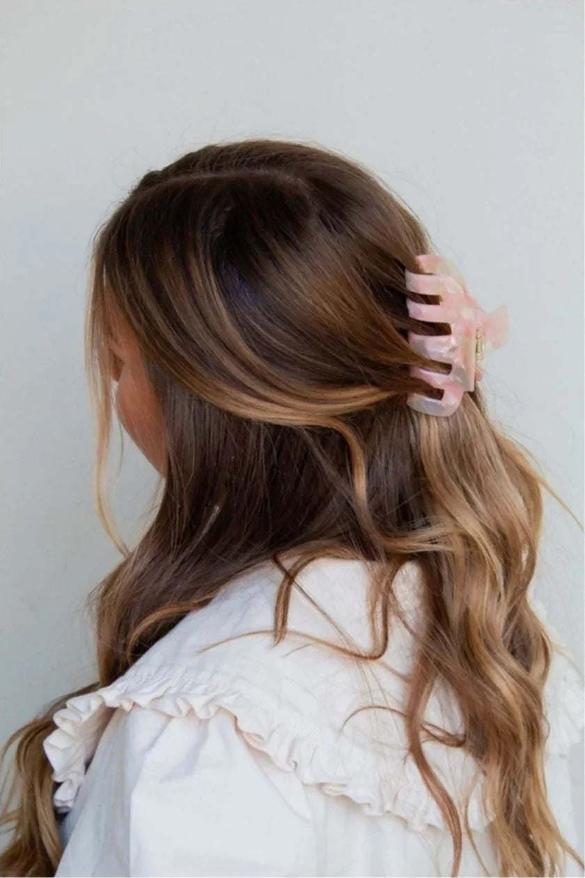 Woman with wavy brown hair wearing a pink claw hair clip and a ruffled white top