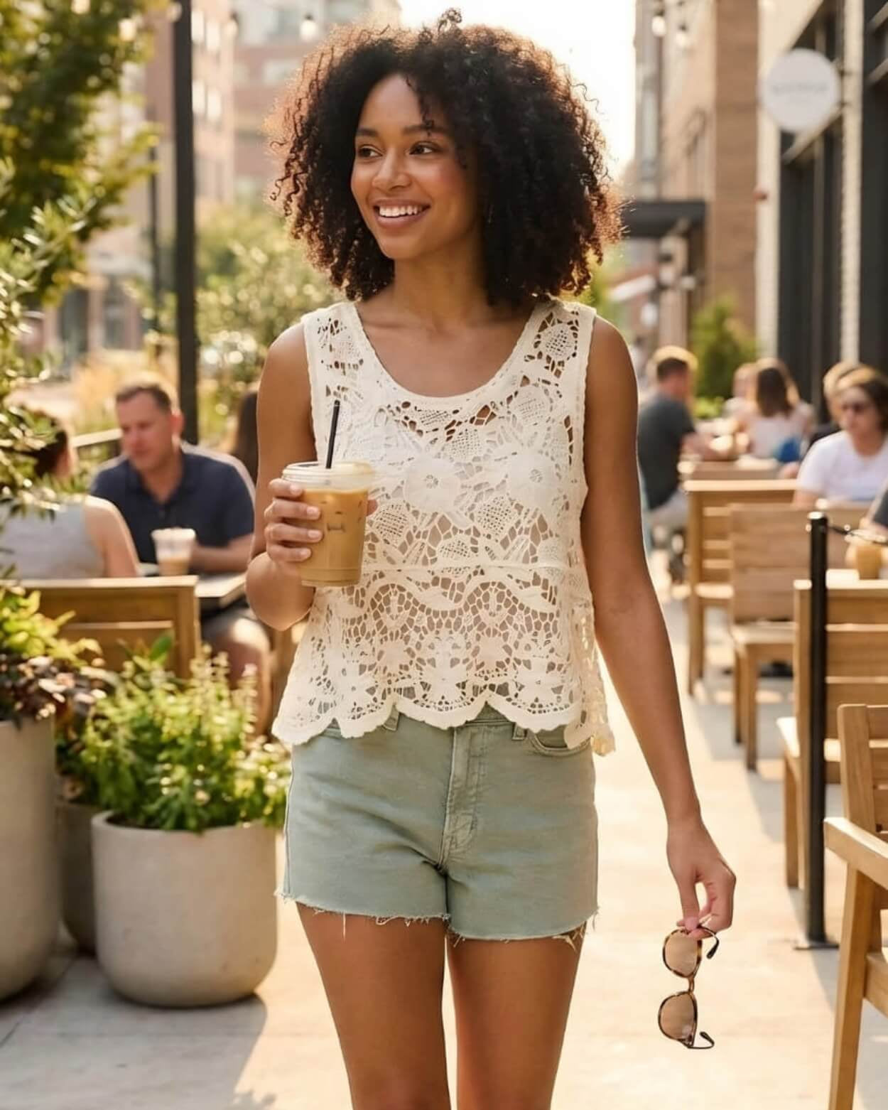 Crochet Lace Tank Top featuring a cream floral crochet lace design with scalloped hem, shown styled with green shorts and holding an iced drink on a sunny street, front walking view.