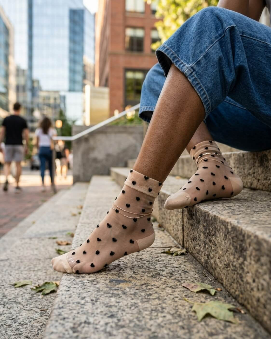 Blushing Hearts Sheer Socks featuring translucent ankle socks with raised black heart accents, soft cuff and toe panels, worn on outdoor stone steps in a city setting, highlighting the sheer texture and playful heart pattern.