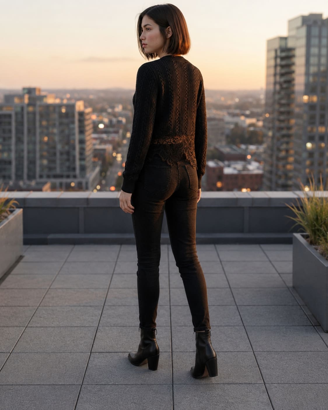 The Eloise Cardigan featuring a textured cable knit design with a scalloped lace hem, shown from the back on a rooftop, highlighting the detailed knit pattern and elegant lace trim.