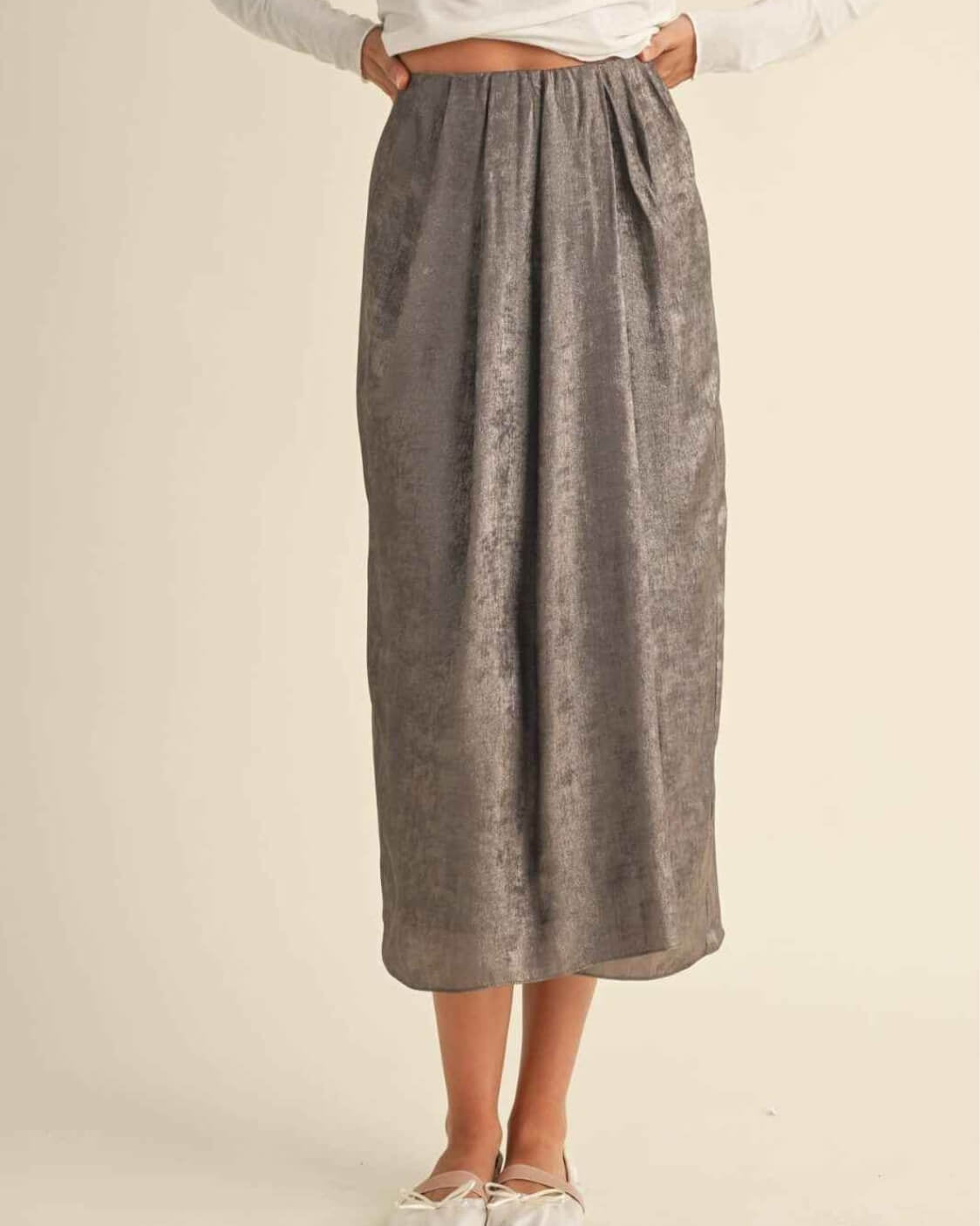 Metallic Fabric Pleat Detailed Skirt featuring a full length flowing structure with soft pleated detailing and metallic inspired texture, styled with ballet flats against a minimal neutral backdrop, highlighting effortless drape and understated sophistication.
