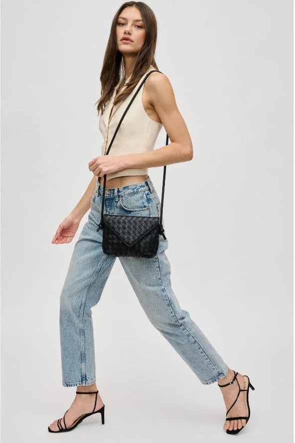Woman in cream sleeveless top, blue jeans, and black heels carrying a black crossbody bag
