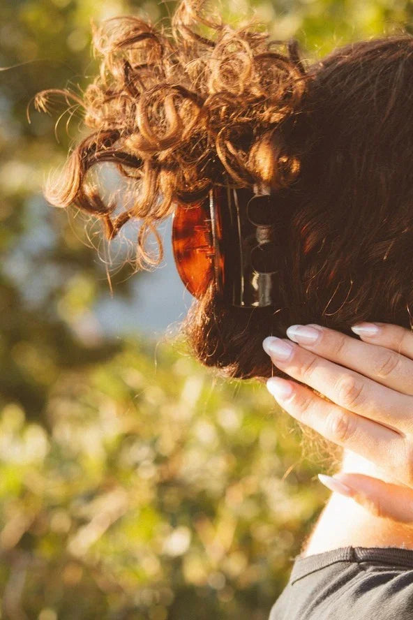Woman with curly hair in a brown claw clip, natural outdoor setting, Love Classic style
