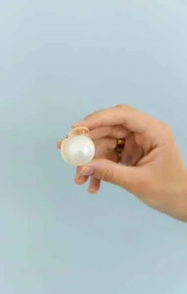 Hand holding elegant large pearl earring against light blue background, Love Classic jewelry