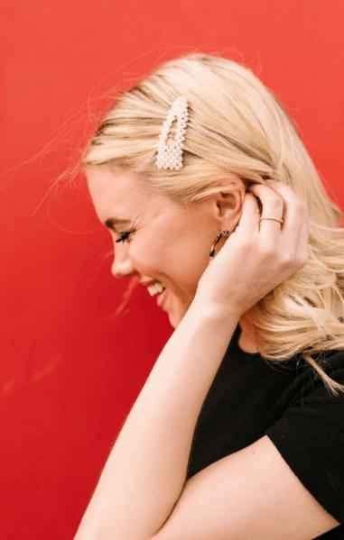 Smiling woman with pearl hair clip and blonde hair in front of a red background, Love Classic style