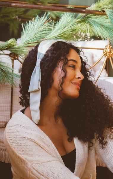 Woman with curly hair wearing white bow headband and cozy sweater, Love Classic style