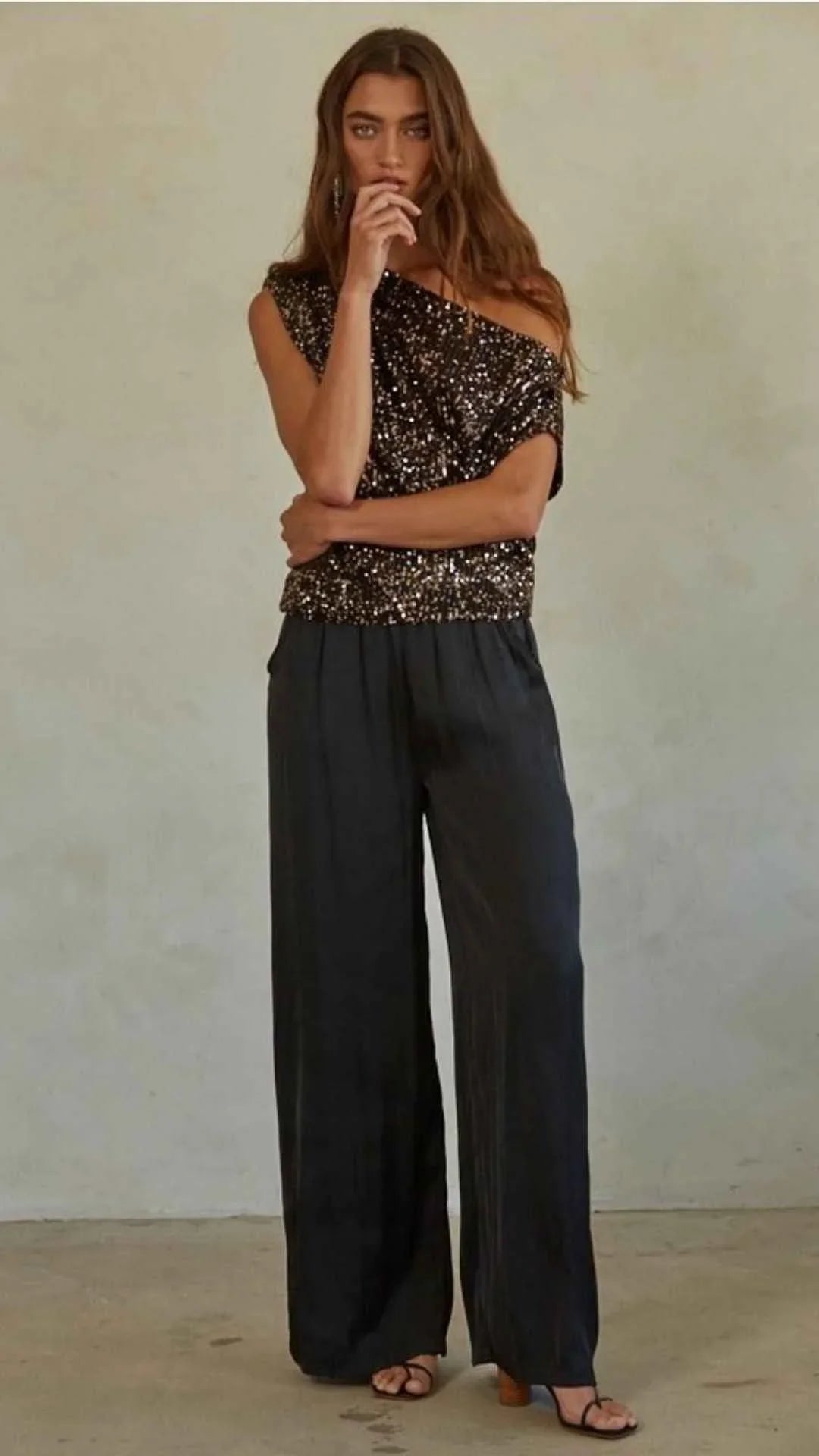 Woman in sparkly black one-shoulder top and wide-leg black pants from Love Classic