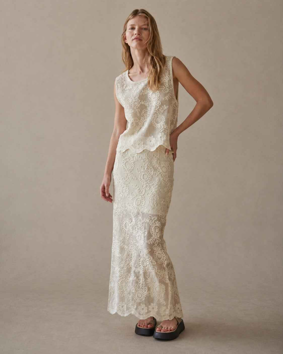 Sleeveless Embroidery Crop Top showcasing allover floral embroidered detailing with a sheer textured finish and scalloped edge hem, paired with a coordinating embroidered maxi skirt in a full-length studio view, emphasizing its effortless silhouette and refined bohemian appeal.