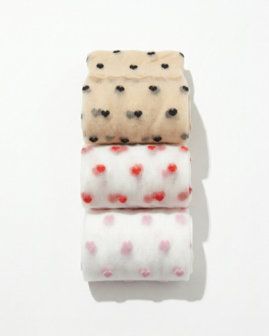 3-Pack Blushing Hearts Sheer Socks featuring folded sheer socks with black heart, red heart and soft dot patterns, stacked neatly on a bright studio surface, highlighting the compact bundle presentation and delicate transparent texture.