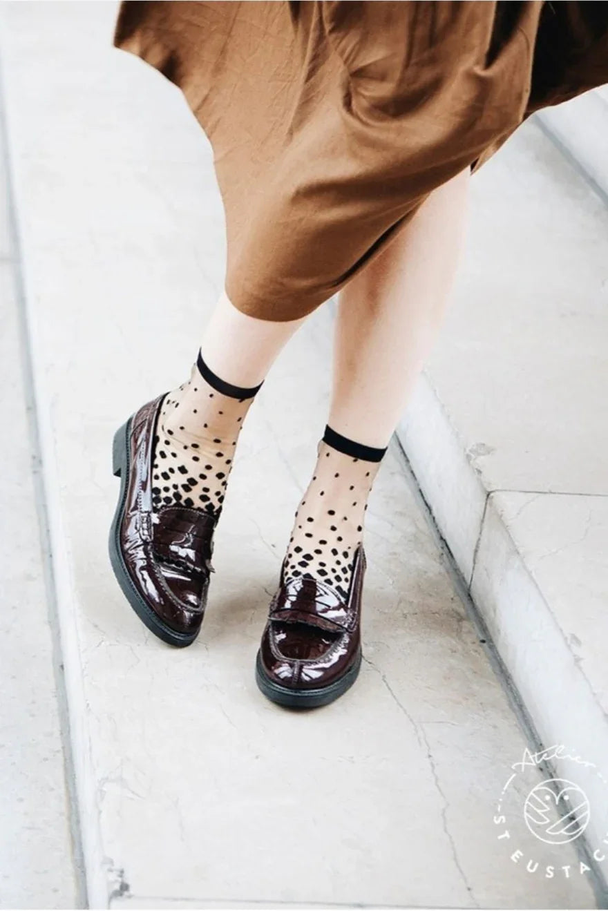 Woman wearing sheer black polka dot socks and shiny patent loafers with a brown skirt