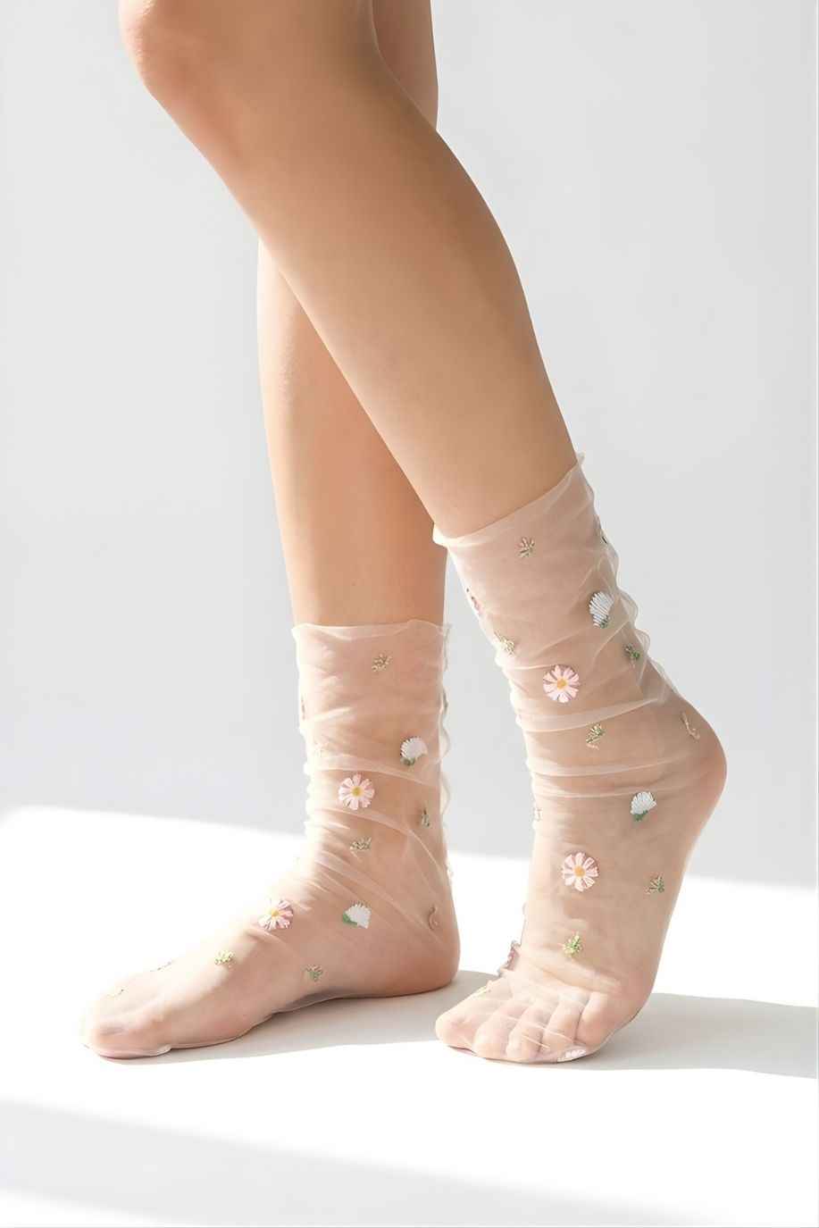 Sheer Garden Daisy Crew Socks in blush nude mesh with embroidered daisy flowers, shown on crossed legs against a clean light background to highlight the transparent fabric.