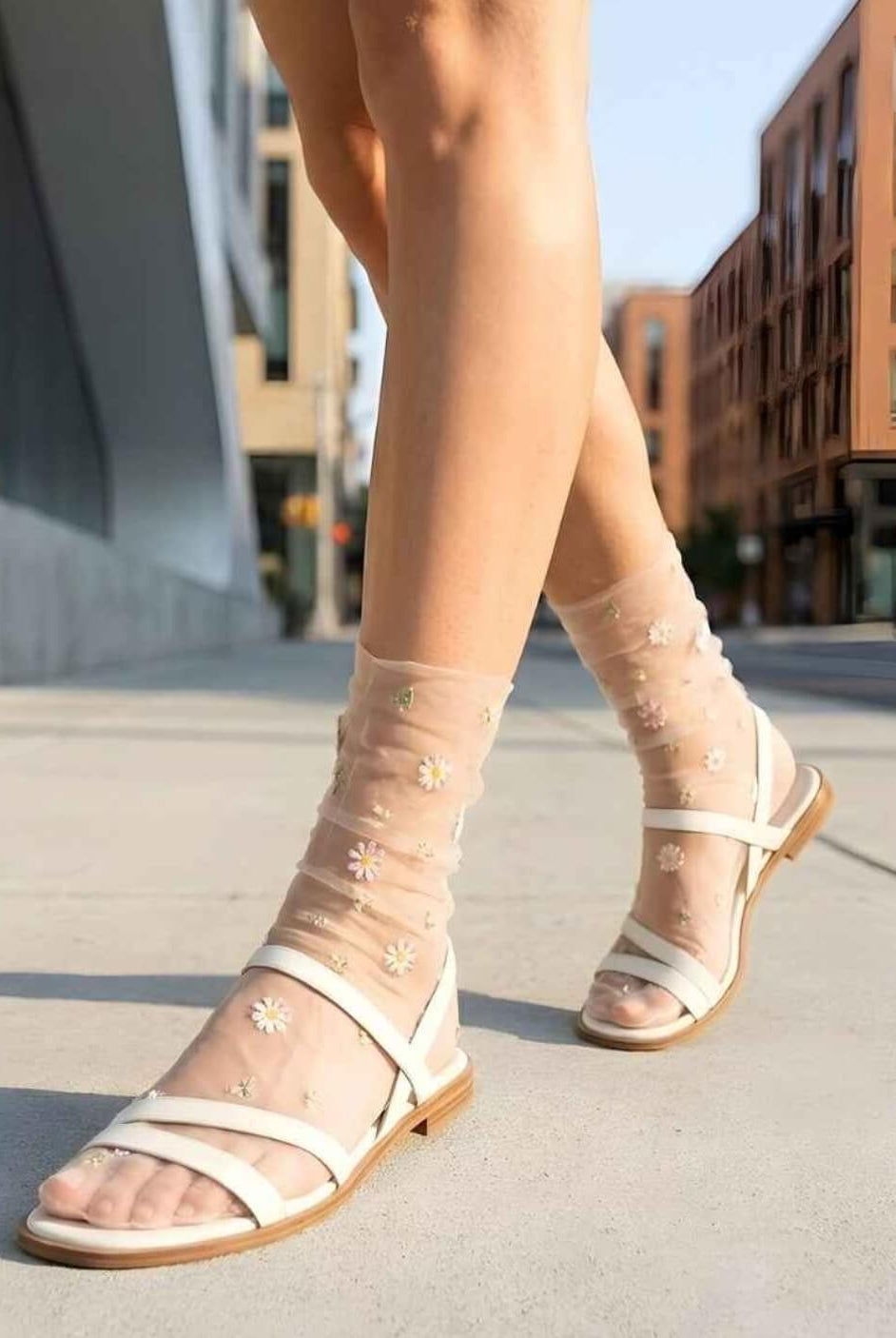 Sheer Garden Daisy Crew Socks in nude sheer fabric with floral embroidery, paired with white strappy sandals while walking on a city sidewalk.
