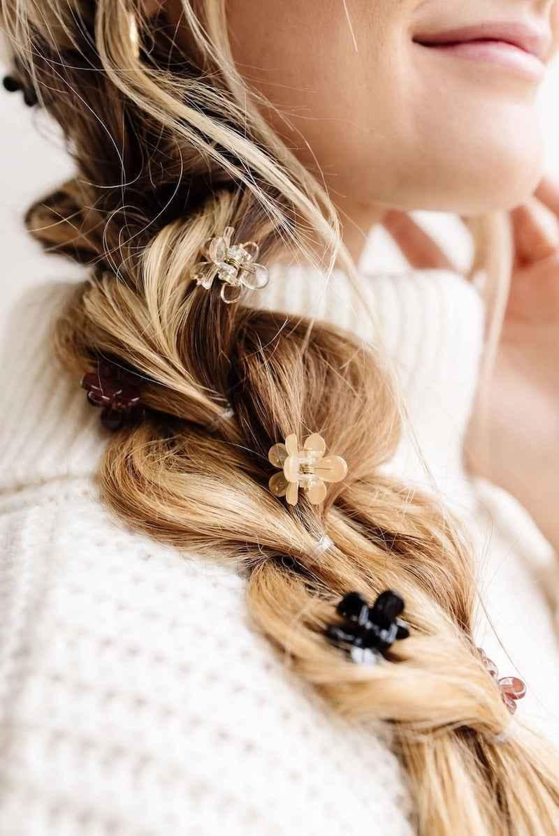 Close-up of braided blonde hair with flower-shaped hair clips, cozy white sweater, Love Classic style