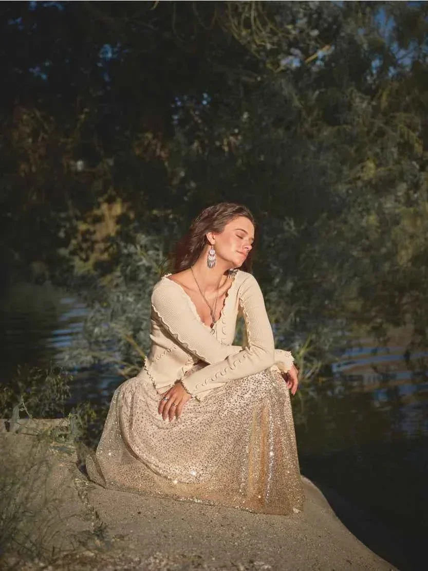 Woman in cream sweater and sequin skirt sitting outdoors by water, Love Classic fashion