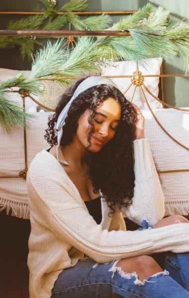 Woman in cozy knit sweater with headband sitting by bed with pine garland, Love Classic style
