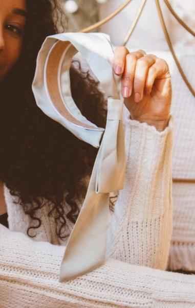 Woman in white sweater holding elegant beige headbands with bow, Love Classic style accessory