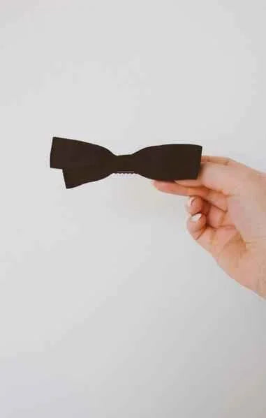 Hand holding a black classic bow tie against a white background, Love Classic style.