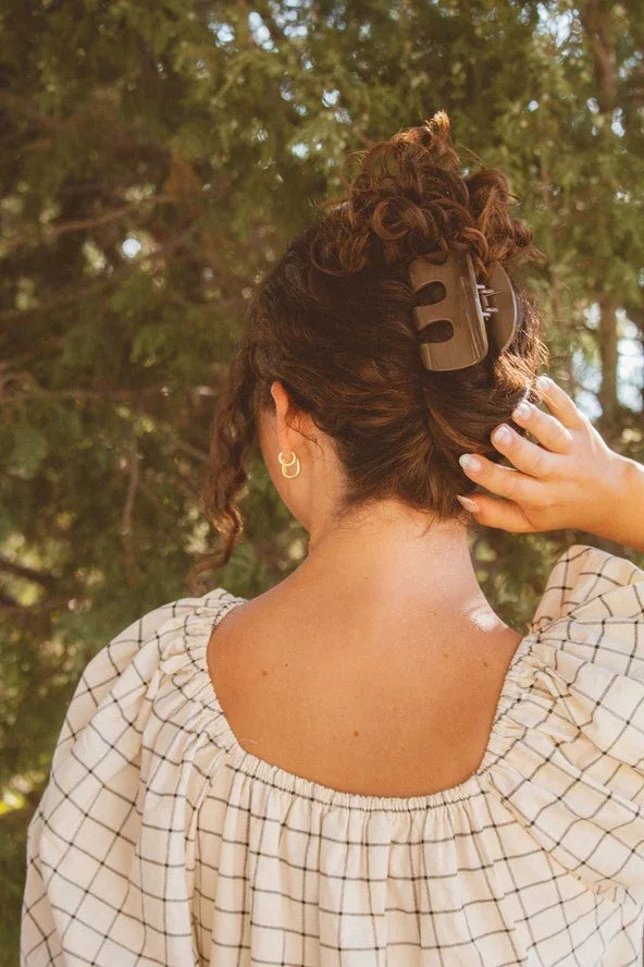 Woman with curly hair in a claw clip, wearing a checked blouse outdoors, Love Classic style