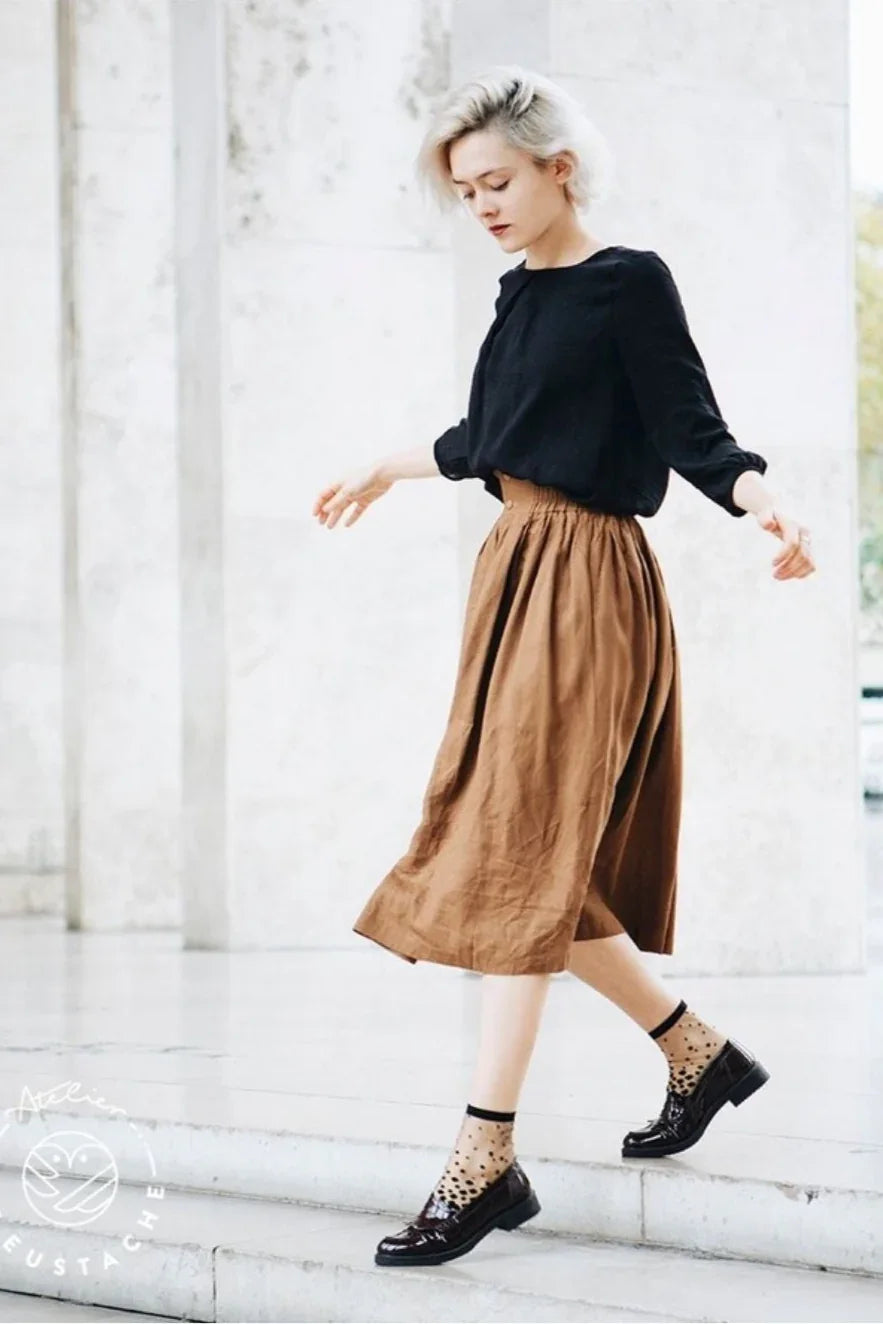 Woman in black blouse and brown midi skirt styling transparent polka dot socks and loafers