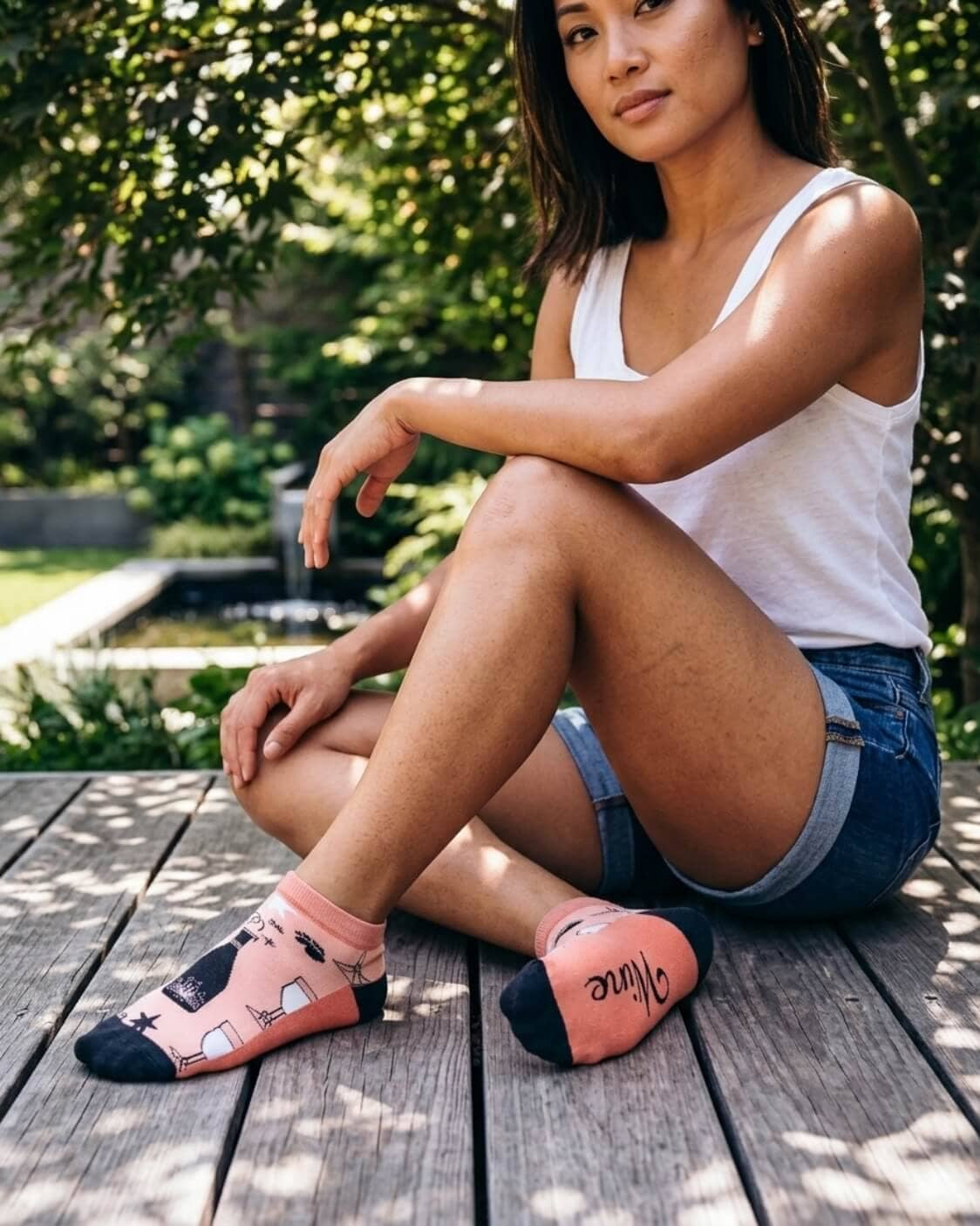 Shorty Socks, Wine Down featuring wine bottle, glass, and corkscrew-inspired graphics with a low cuff and contrast toe panels, worn while seated on a wooden deck, highlighting the fun print and easy everyday comfort.