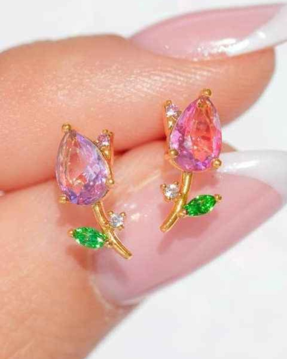 Blossoming Tulip Studs featuring pink teardrop crystal tulip detailing with green leaf accents and polished gold tone stems, held in a close up hand styling shot, highlighting sparkling facets and delicate floral craftsmanship.