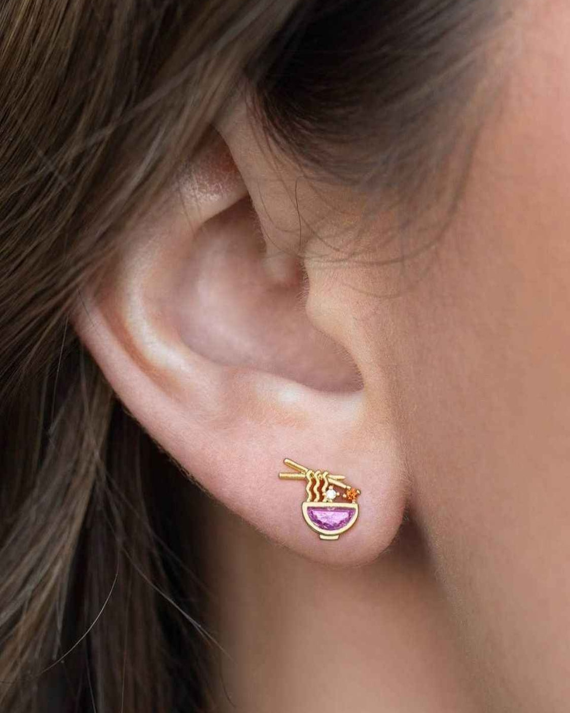 Ramen Studs featuring colorful ramen bowl inspired detailing with crystal accents and chopstick shaped elements, worn in a close up ear styling shot against soft natural lighting, highlighting quirky charm and unique statement jewelry appeal.