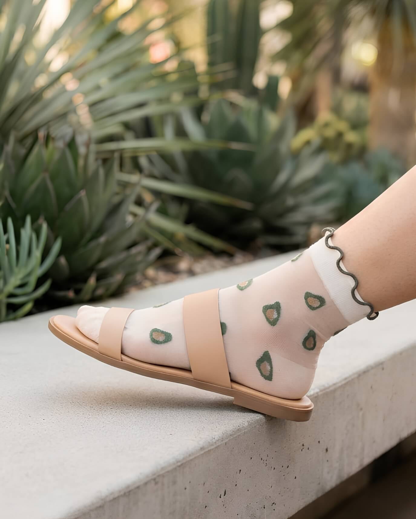 Whimsical Ruffle Edge Sheer Socks featuring translucent mesh fabric with avocado-inspired embroidered accents and scalloped cuff trim, paired with open sandals in an outdoor garden setting, highlighting airy comfort and playful styling versatility.