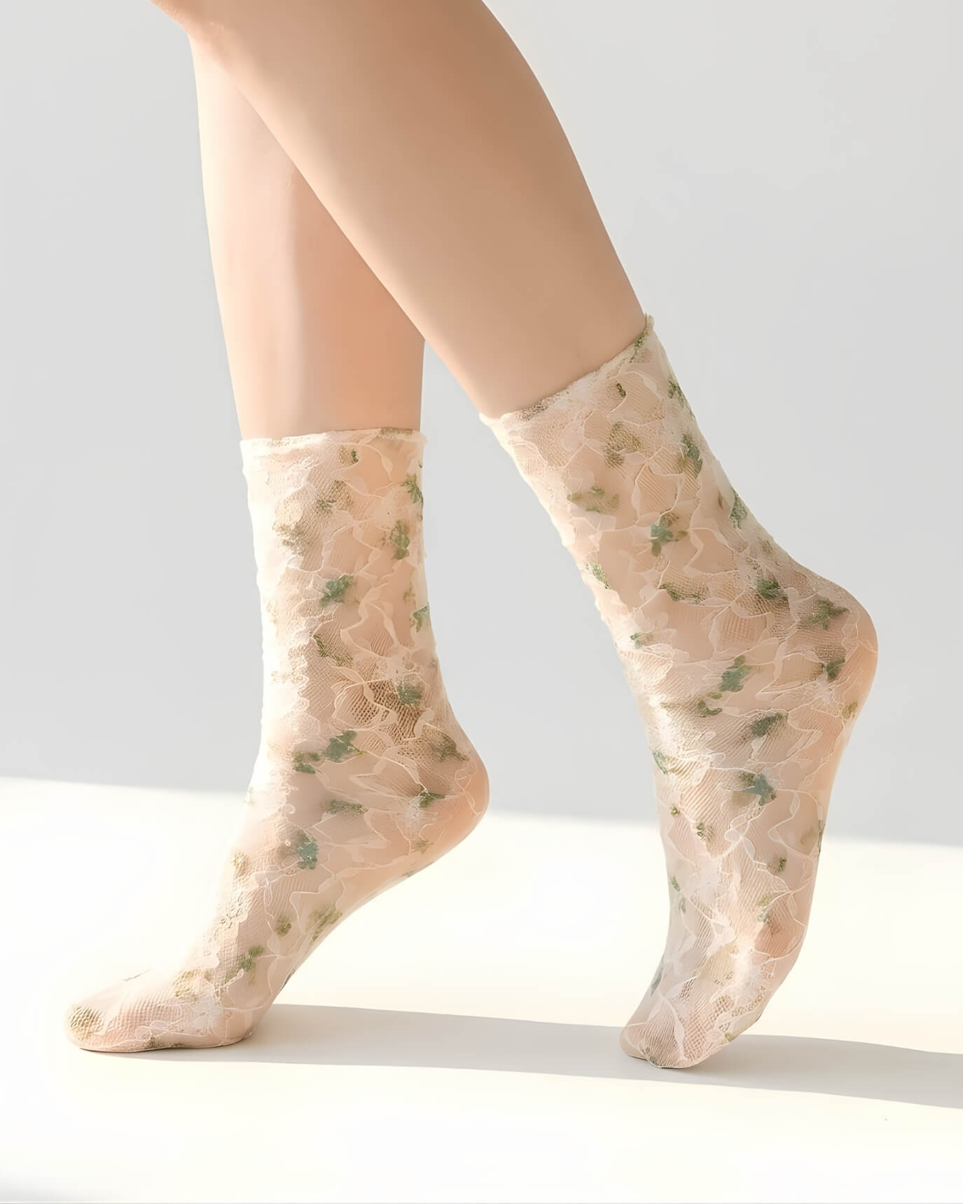 Floral mesh sheer socks in a muted green floral pattern, styled on both feet in a clean studio setting to highlight the soft mesh fabric and delicate lace details.
