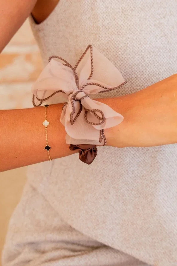Elegant woman's arm wearing a sheer bow scrunchie and gold bracelet, Love Classic style