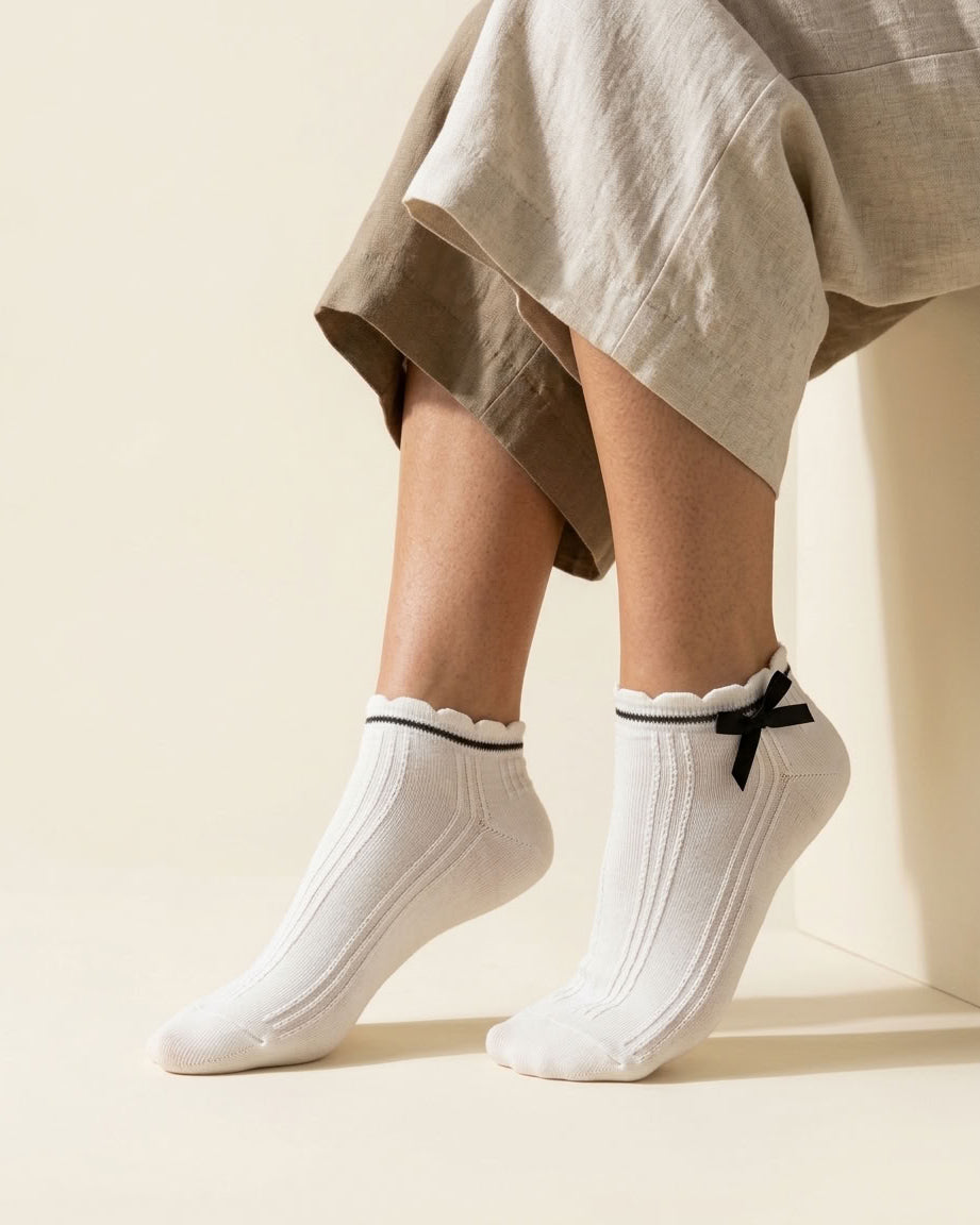 White ribbed ankle socks with scalloped cuff, black stripe and black satin bow, close-up on tiptoe