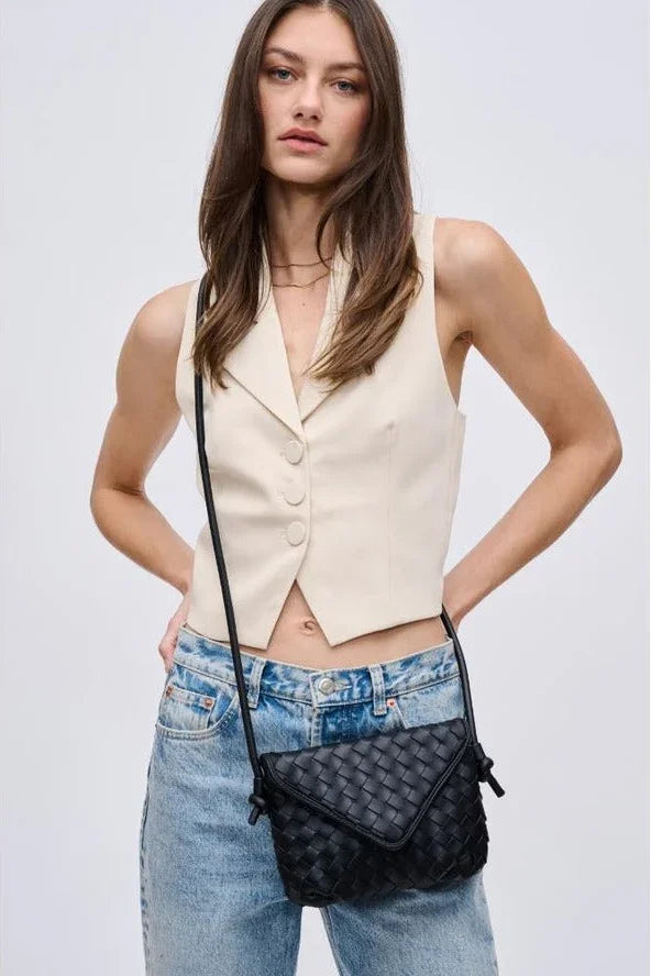 Woman wearing a cream vest, blue jeans, and a black woven crossbody bag from Love Classic