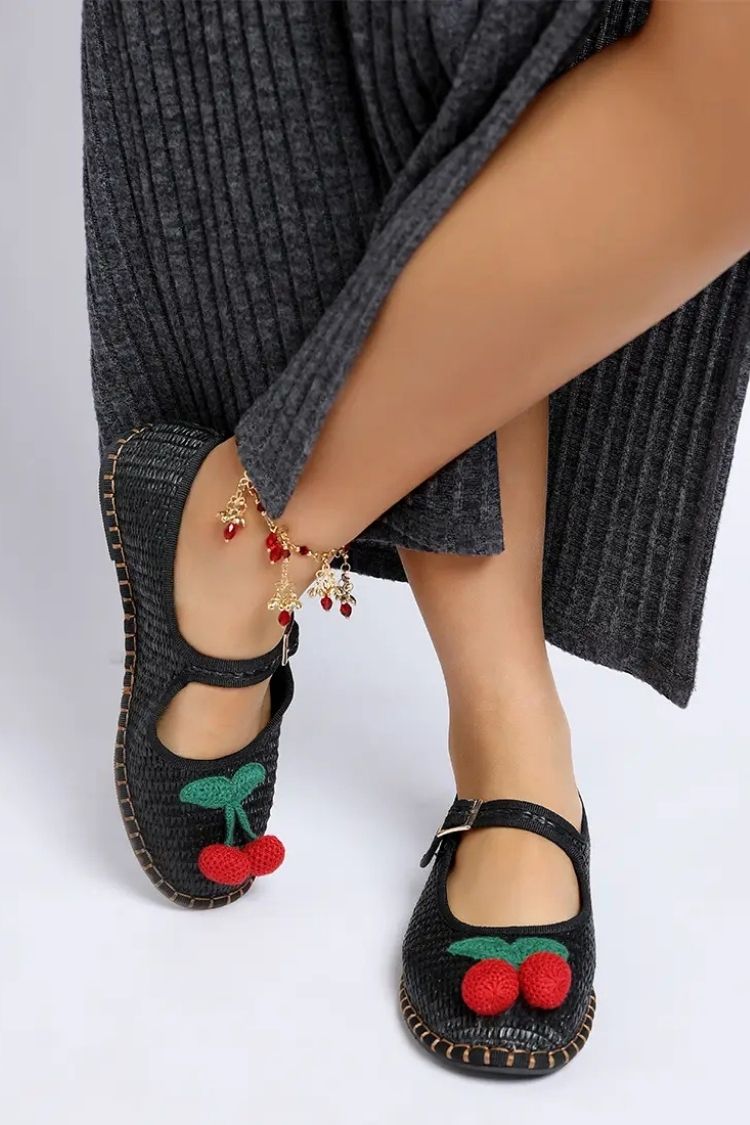 Cherry Accent Mary Jane Flats, black woven Mary Jane flats with red cherry embellishment and buckle closure, styled with a grey dress and statement anklet, highlighting close-up details and craftsmanship.