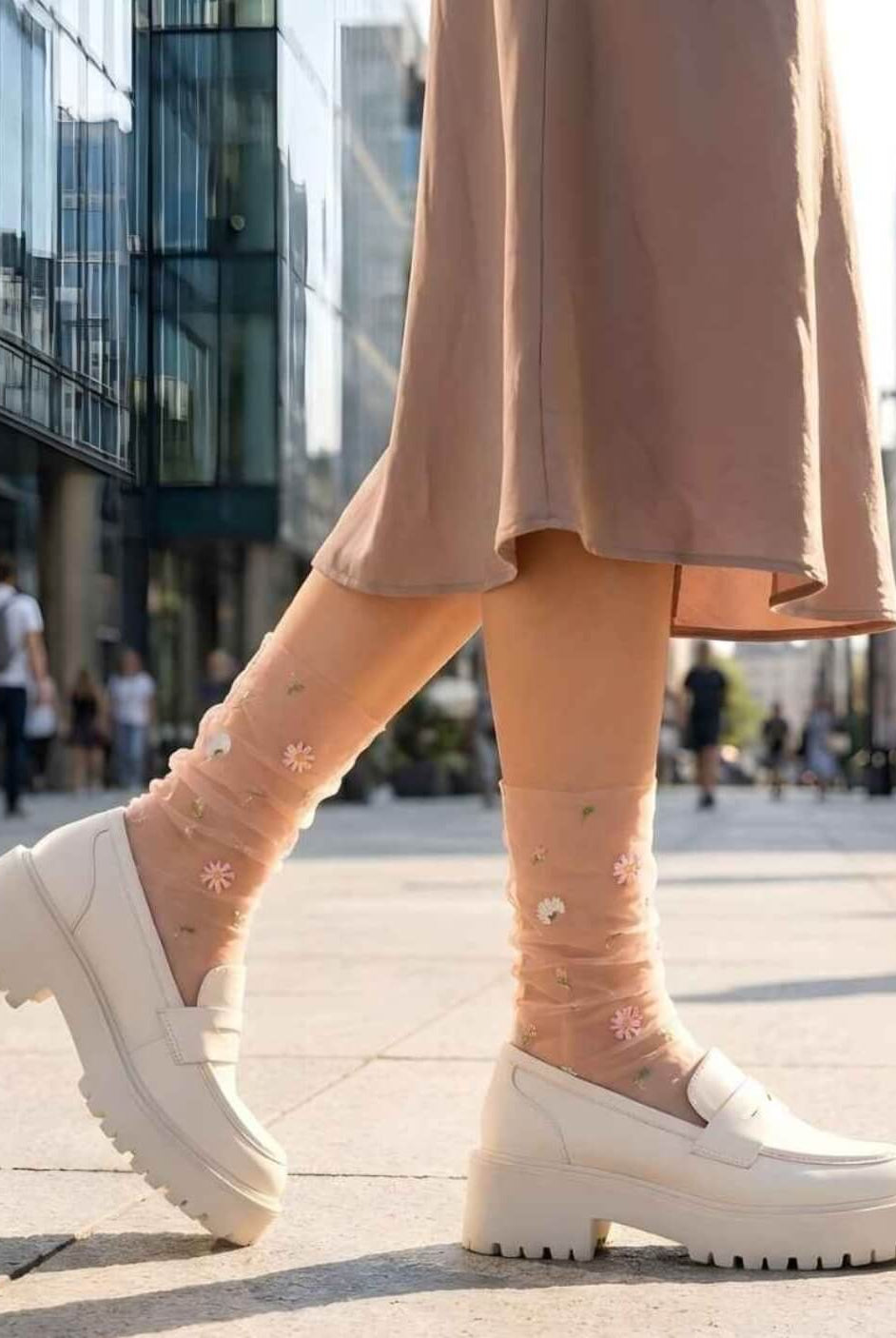 Sheer Garden Daisy Crew Socks in nude with daisy embroidery, styled with white platform loafers in an outdoor city setting for a casual look.