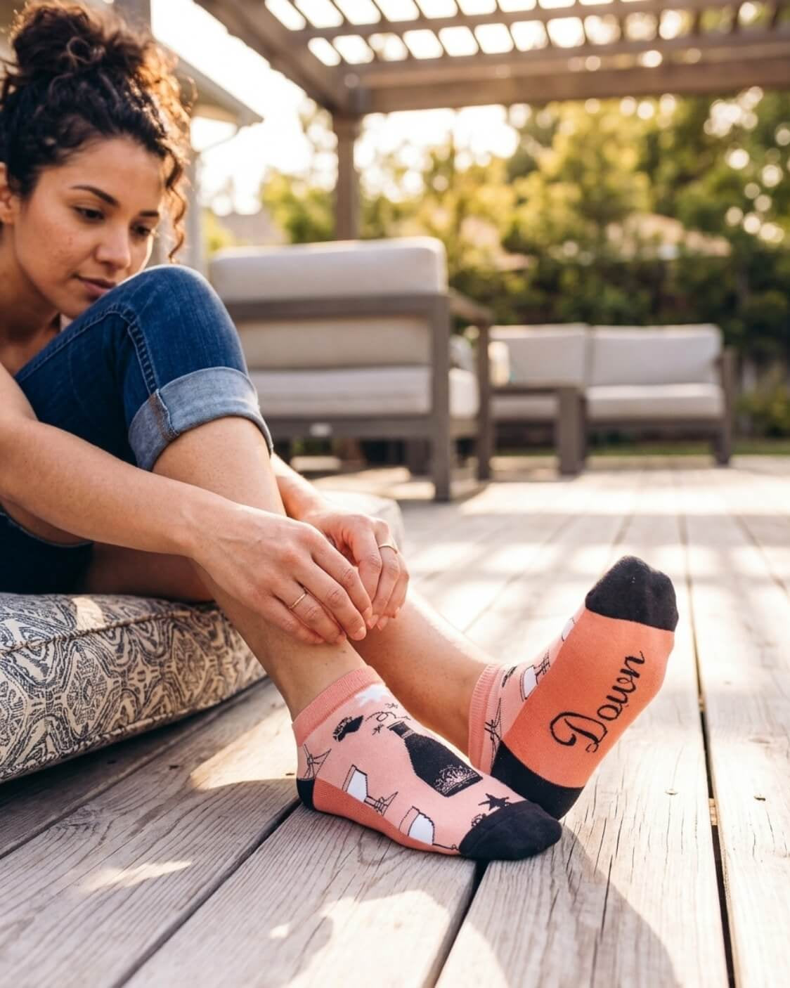 Shorty Socks, Wine Down featuring a short ankle cut, wine-themed pattern, dark toe accents, and “Down” text on the sole, worn while adjusting the cuff on a patio deck, highlighting the graphic sole and snug fit.
