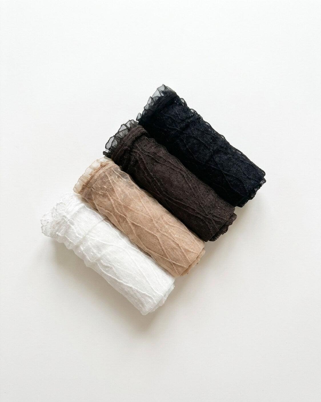 Bundled Packs Rosalie Lace Sheer Socks featuring a lightweight sheer finish with textured lace patterning and ruffled cuff edges, arranged in a diagonal rolled stack on a minimal studio surface, highlighting the pack assortment and delicate feminine styling.