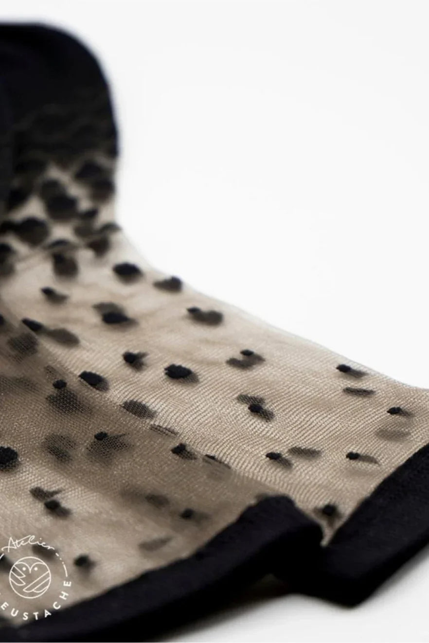 Sheer mesh fabric with black polka dots and solid black trim, close-up view