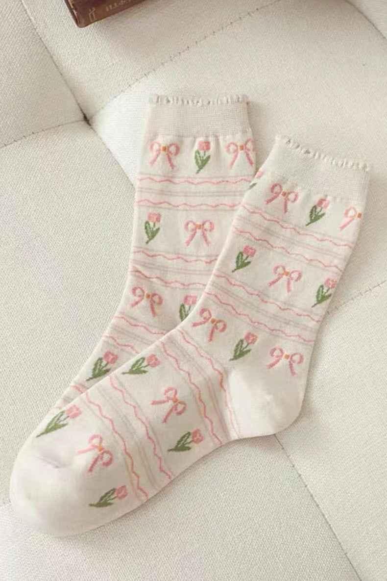 Cream socks with pink bows and flower pattern on a beige couch, Love Classic style